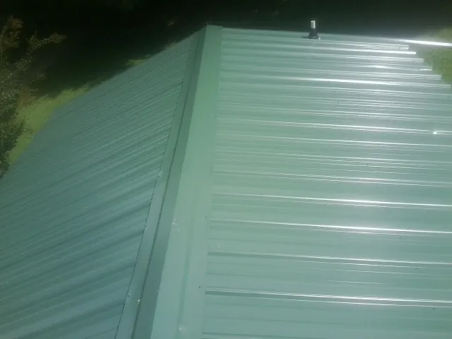 New green metal panels meeting at the ridge of a roof — Flat Roof Repair work by our crew in Pekin