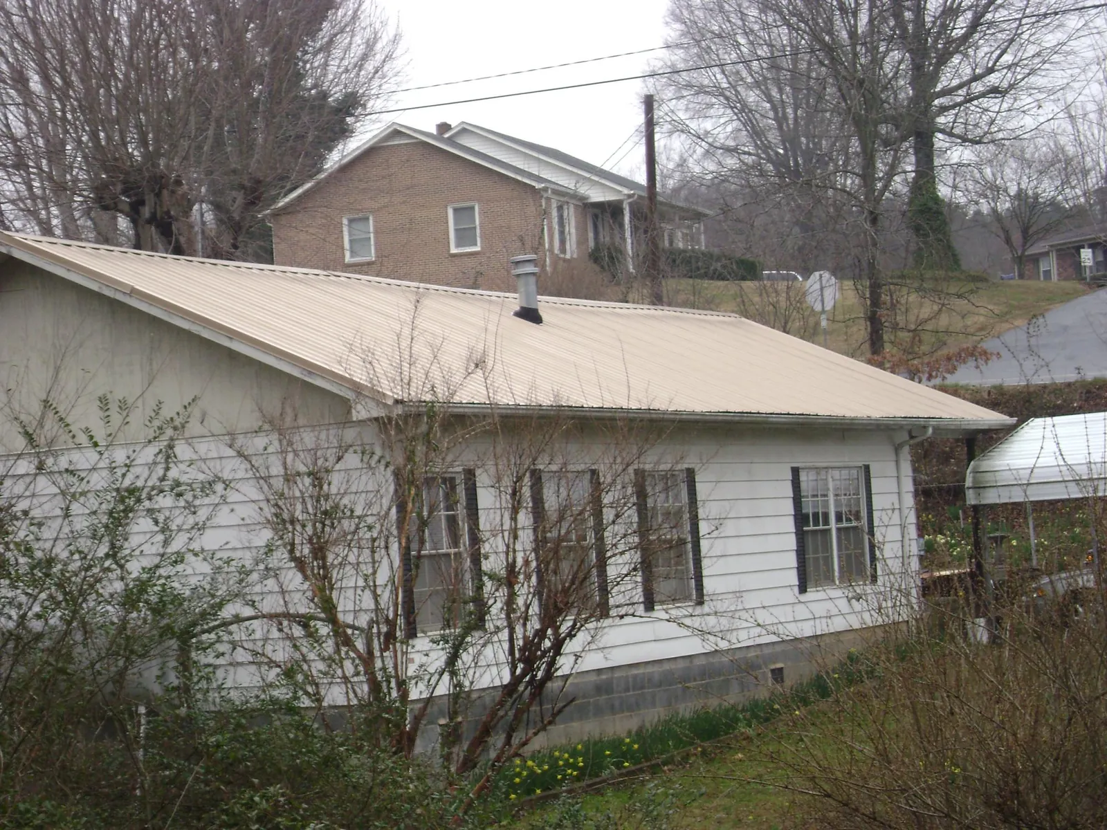 Tan metal roof on a white sided house set into a hillside — Commercial Roofing by Roofing Brothers in Pekin