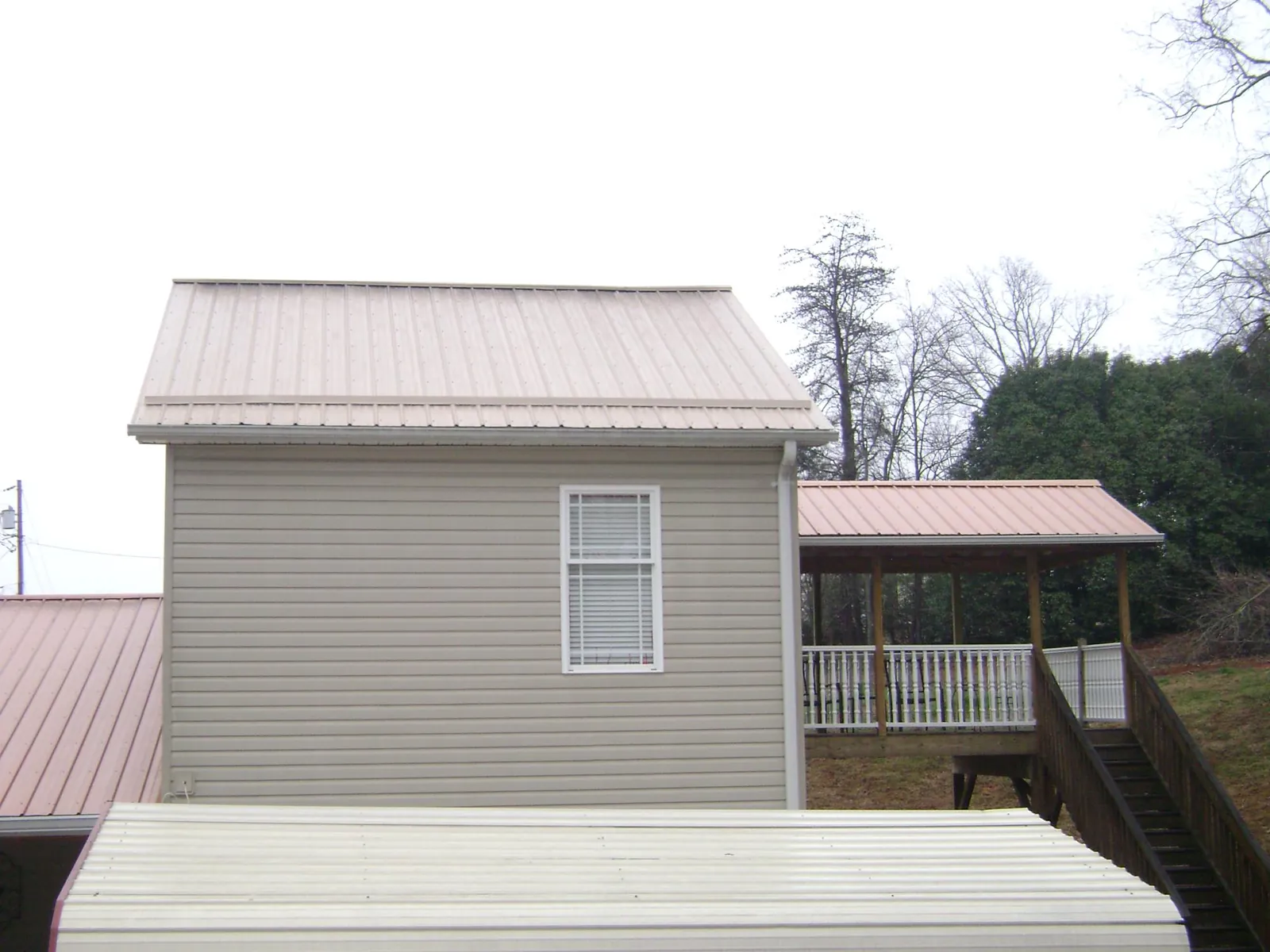 Tan metal roofs on a two story addition and attached porch, from a Roof Replacement job in Pekin
